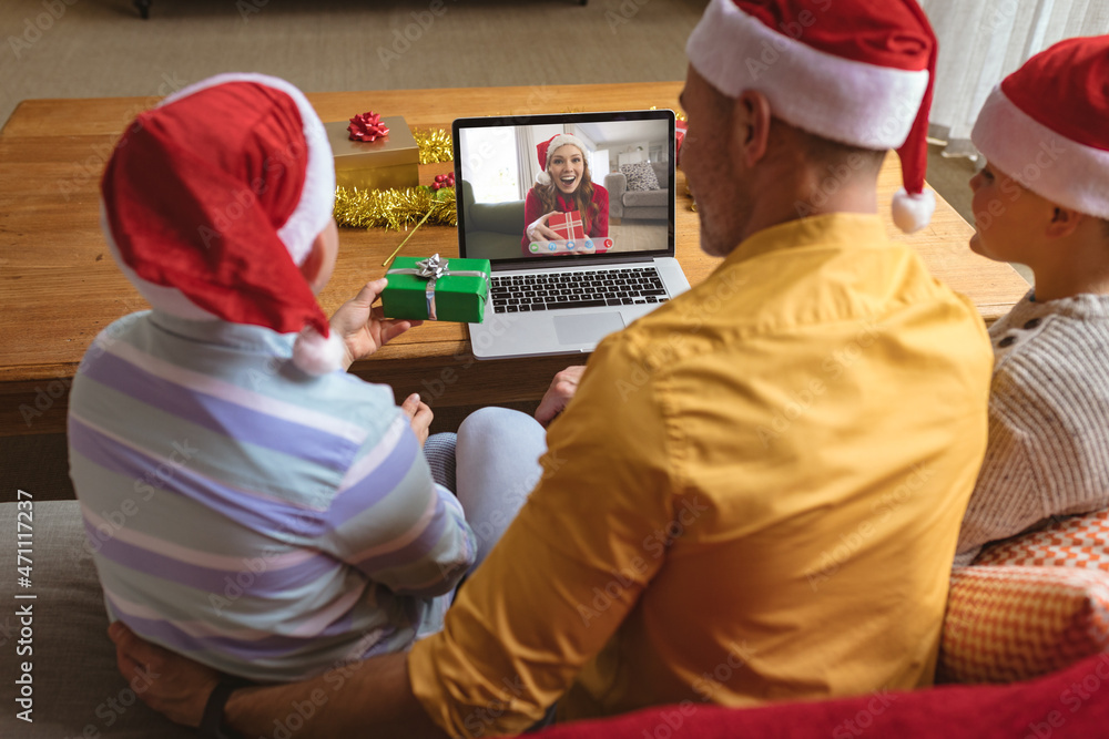 戴着圣诞老人帽的白人父子与兴奋的女人进行笔记本电脑圣诞视频通话