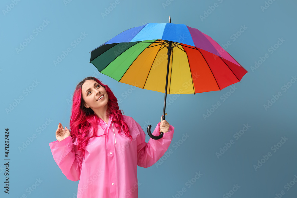 美丽的女人穿着雨衣，彩色背景上带着雨伞