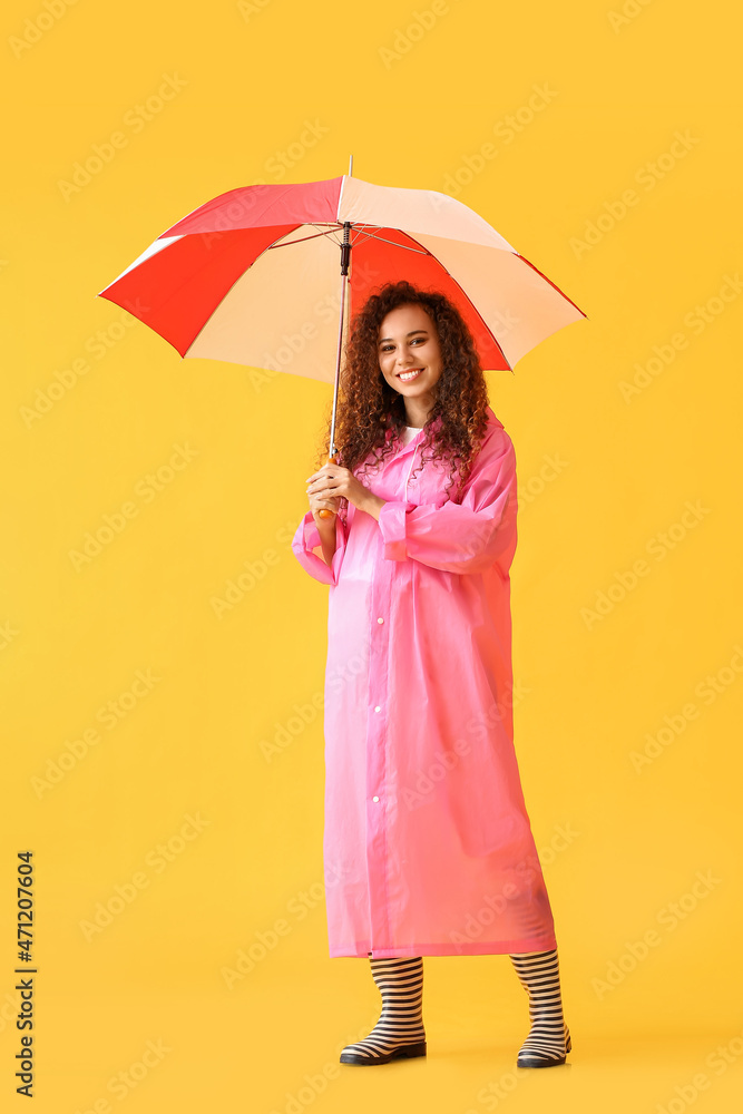 年轻的非裔美国妇女穿着粉色雨衣和秋葵靴，黄色背景带雨伞