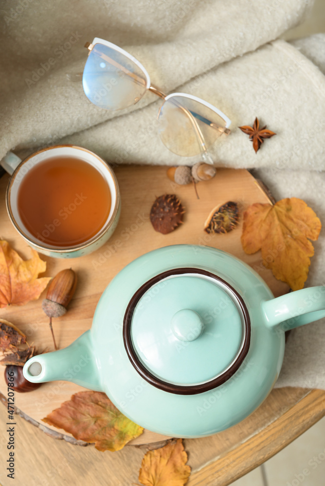 房间桌子上的茶壶、一杯热饮、眼镜和秋叶