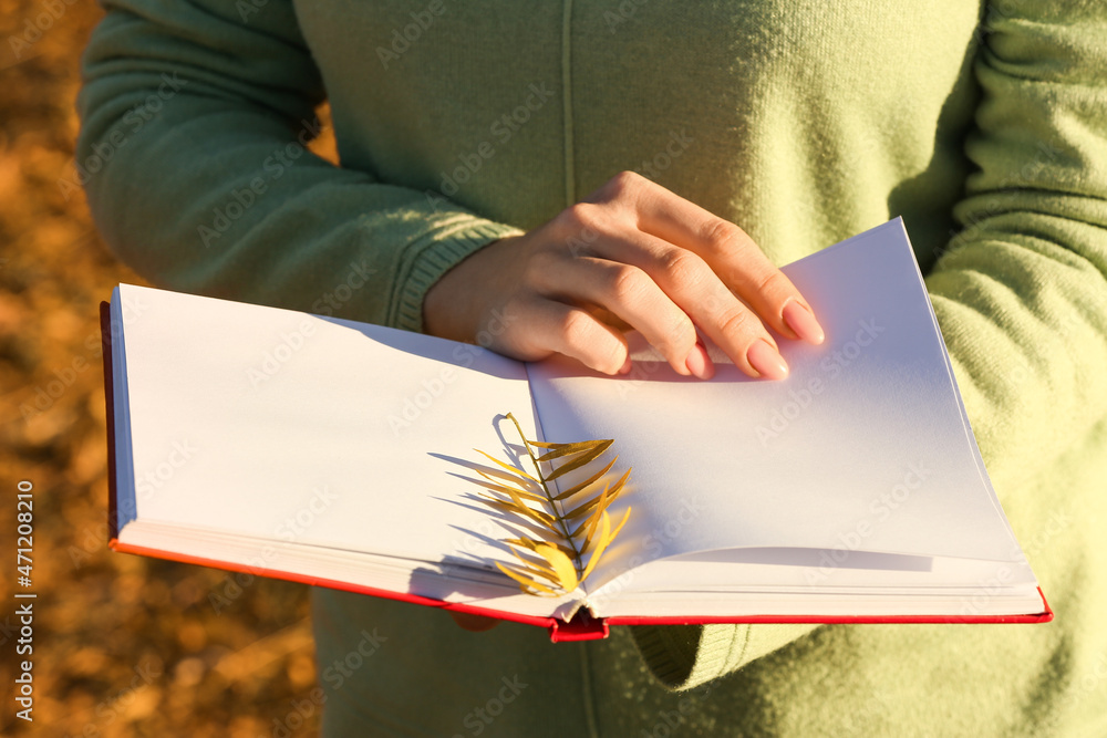 阳光明媚的日子里，女人拿着一本秋叶打开的书，特写