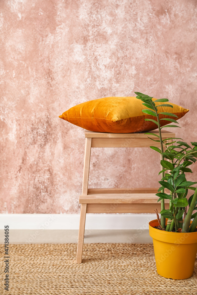 粉色墙壁附近带枕头和室内植物的木制台阶凳