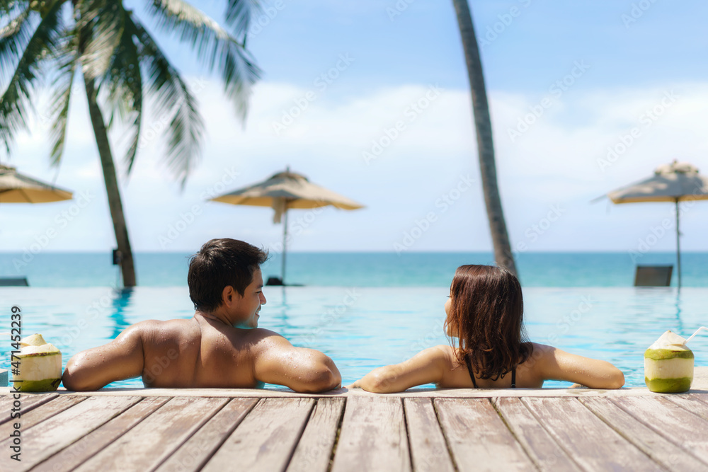 夏季旅游度假概念，亚洲情侣带着椰子在豪华无边泳池放松
