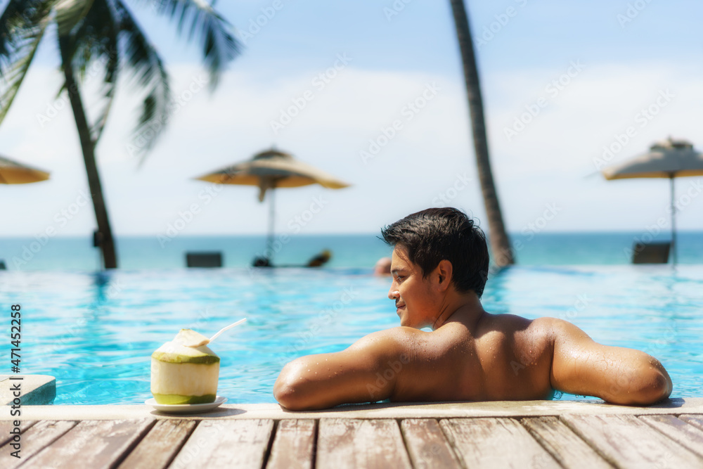 夏季旅行度假概念，亚洲旅行者带着椰子在豪华无限泳池酒店放松身心