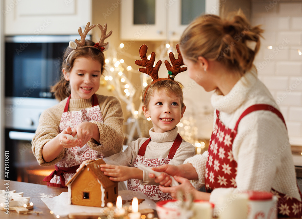 幸福的家庭母亲和两个孩子穿着圣诞围裙装饰圣诞蜂蜜姜饼屋