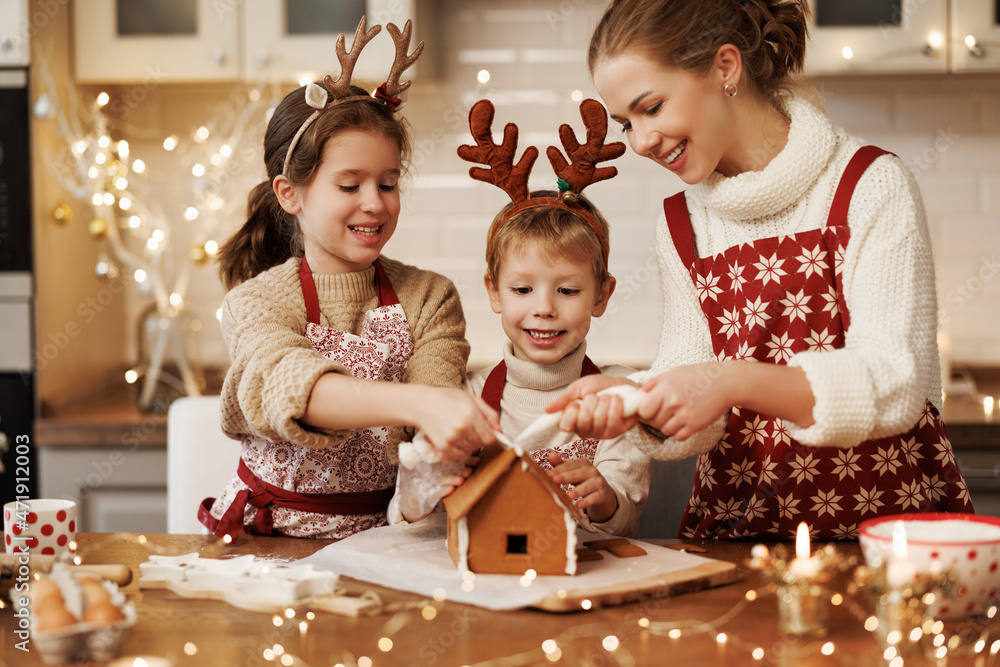 幸福的家庭母亲和两个孩子穿着圣诞围裙装饰圣诞蜂蜜姜饼屋