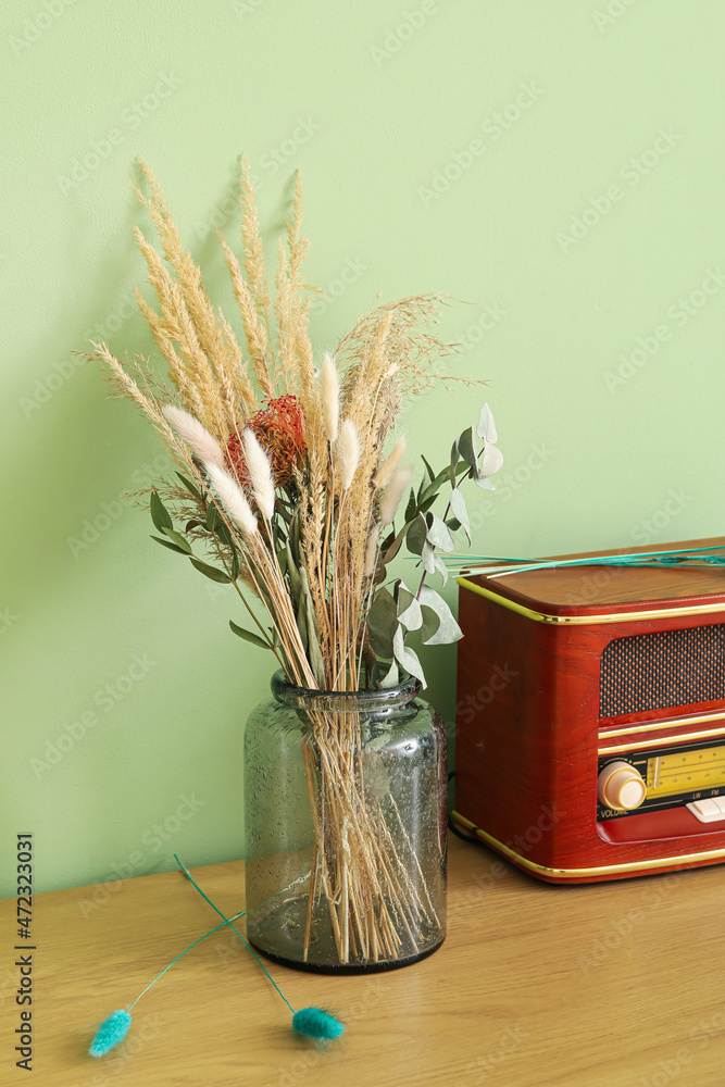 绿色墙壁附近桌子上的花瓶，上面有干花和复古的无线电接收器