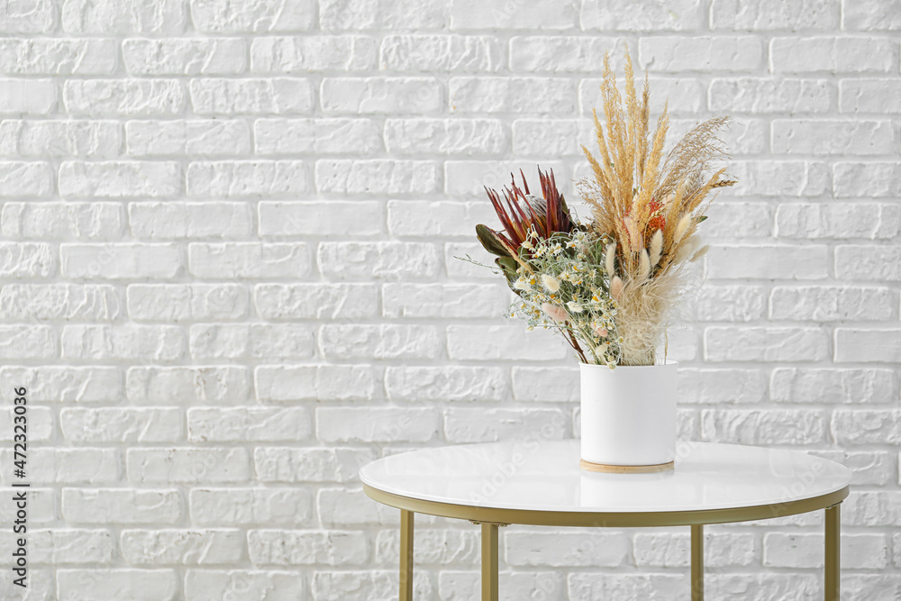 白色砖墙附近桌子上放着干花的花瓶