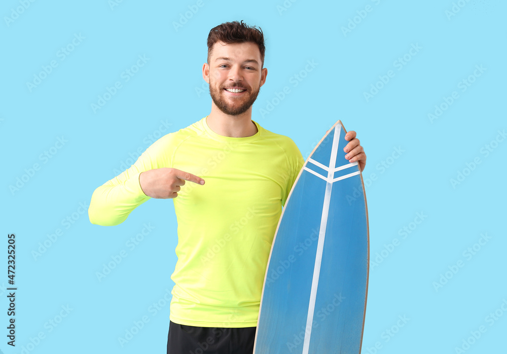 蓝色背景下英俊的胡子男子指着冲浪板