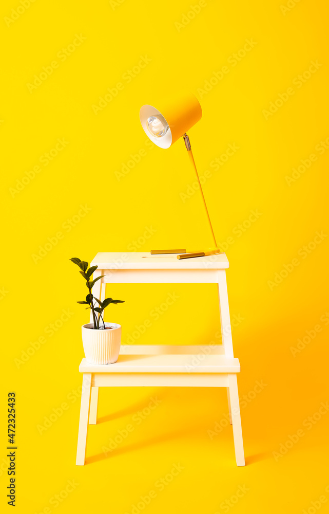 黄色背景带灯和花盆的白色脚凳