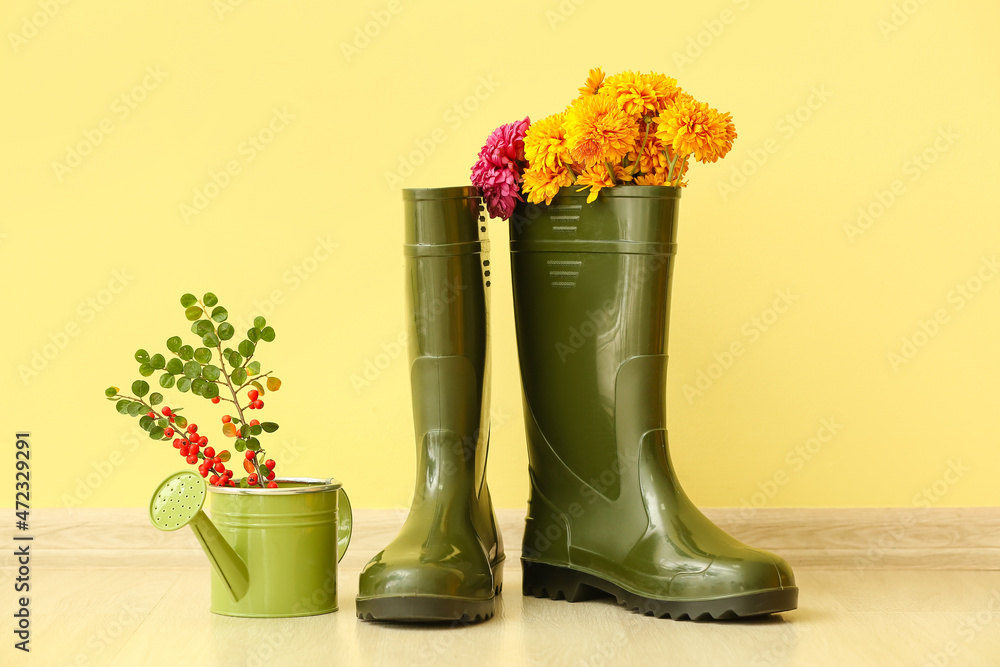 一双橡胶靴、鲜花和喷壶贴在彩色墙上