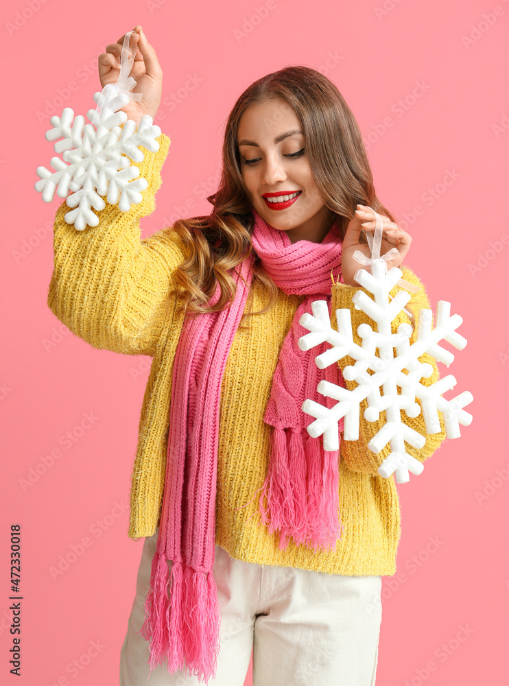 微笑的女人穿着暖和的衣服，手里拿着彩色背景上的大雪花