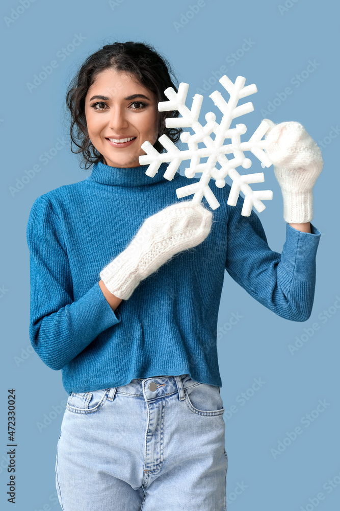 身穿冬装的微笑女人，蓝色背景下拿着一片雪花