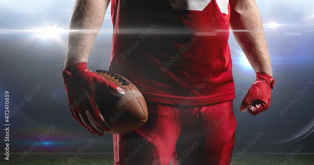 美国足球运动员穿着红色球衣，戴着手套在球场上持球的中段