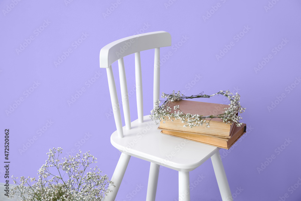 Modern chair with books and flowers near color wall