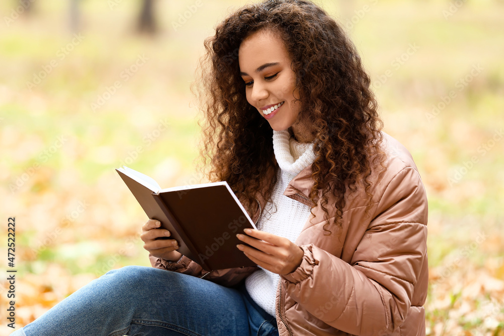 美丽的非裔美国妇女在秋季公园看书