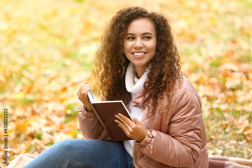 微笑的非裔美国妇女在秋季公园拿着书