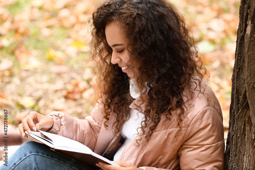 美丽的非裔美国妇女在秋季公园读书
