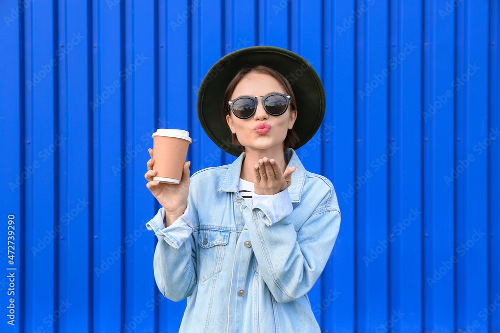 时尚女人拿着纸杯茶，在蓝色背景上飞吻