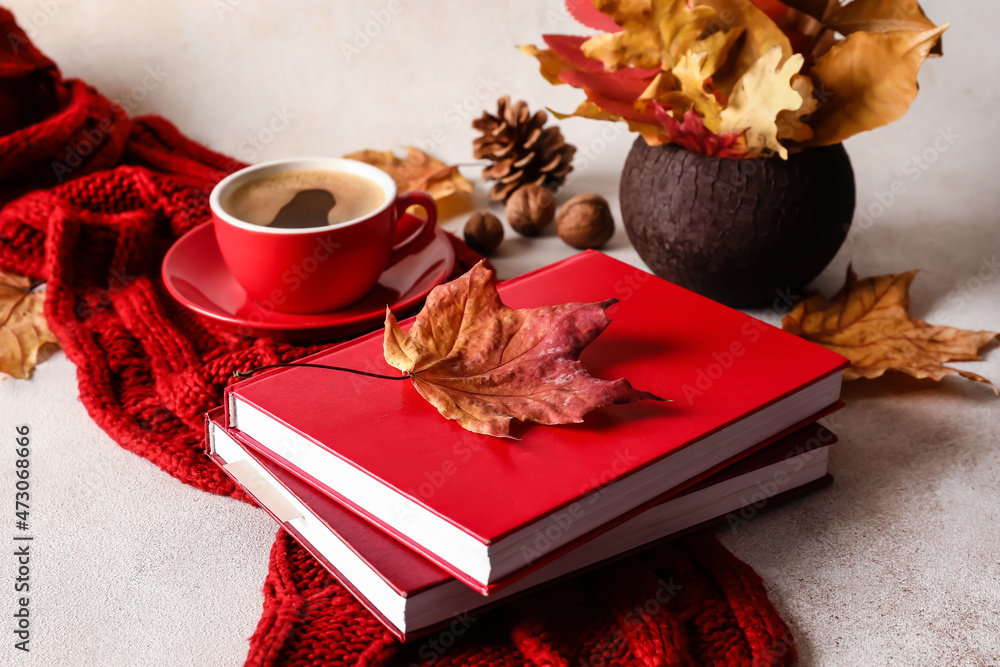 一摞书、一条针织围巾、一杯咖啡和一个放在浅色桌子上的秋叶花瓶