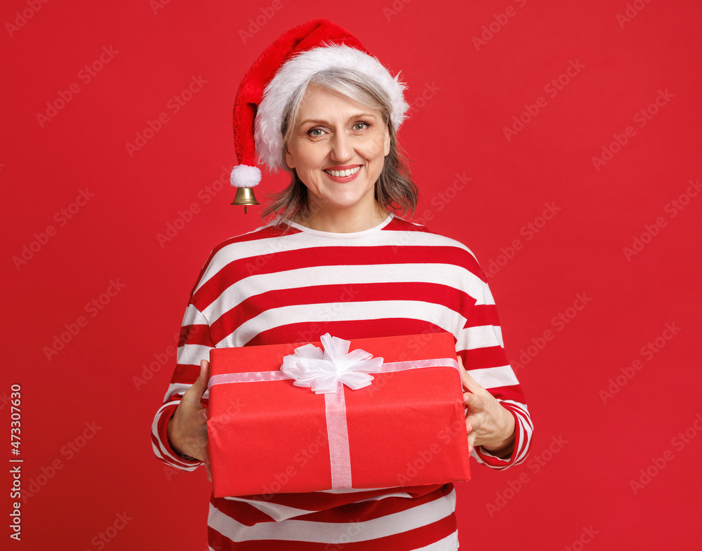 戴着红色圣诞帽的快乐惊讶的高级女性拿着圣诞礼物，笑着带着有色人种