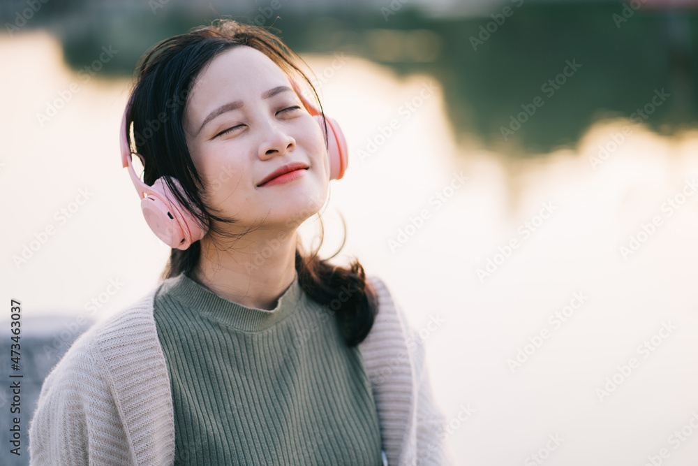 美丽的亚洲女孩在湖边听音乐