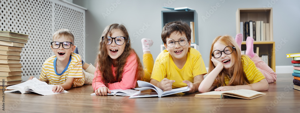 四个戴眼镜的可爱孩子拿着书躺在室内地板上