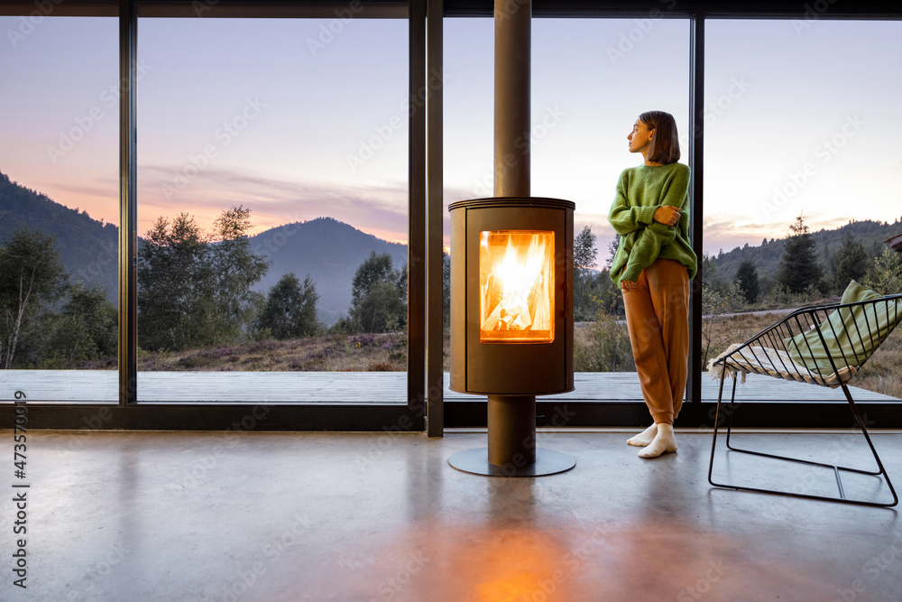 Woman enjoy great view on mountains while sitting near fireplace at modern living room at sunset . C