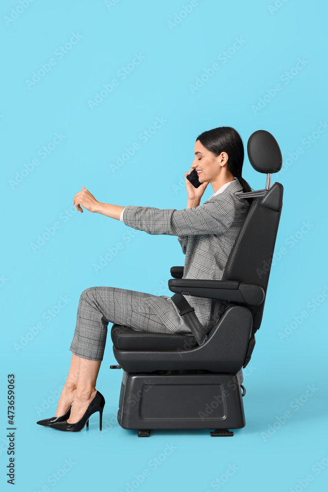 蓝色背景下坐在汽车座椅上，拿着方向盘的年轻女子在讲手机