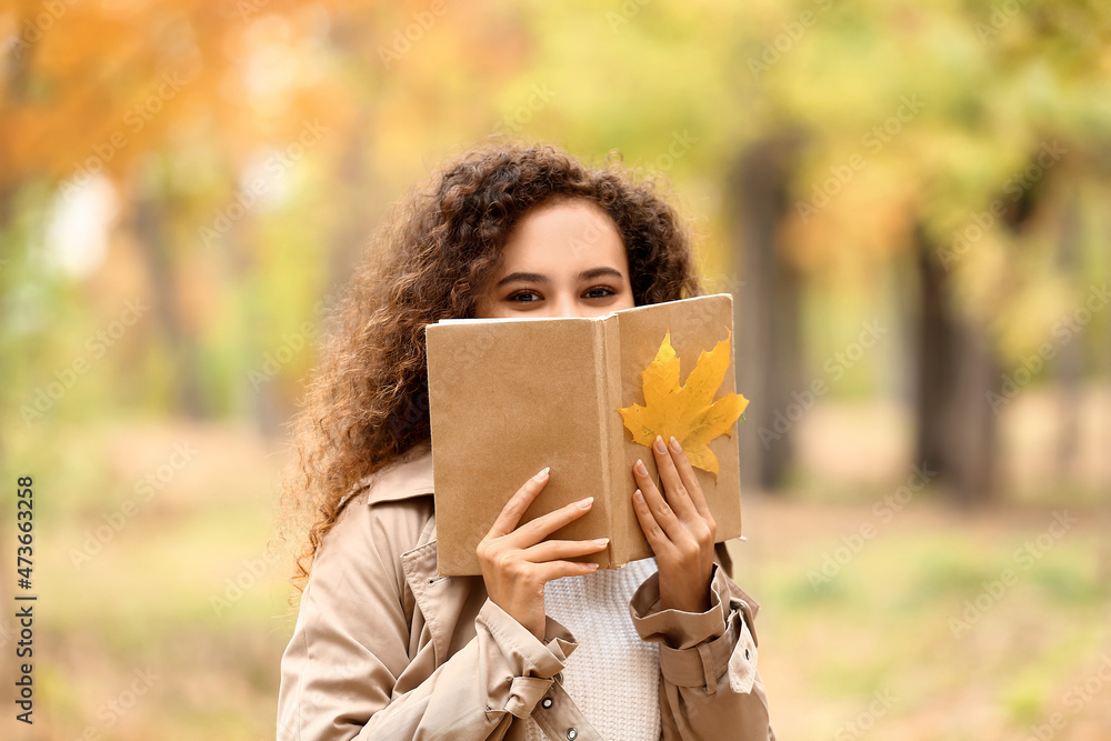 秋天公园里年轻的非裔美国妇女拿着书和干树叶的画像