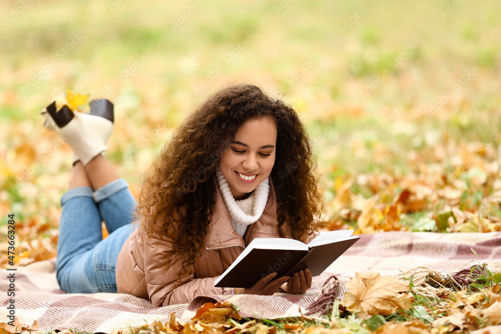 年轻的非裔美国妇女在秋季公园阅读关于格子花纹的书