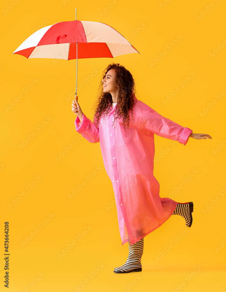 年轻的非裔美国妇女穿着粉色雨衣和秋葵靴，黄底带伞