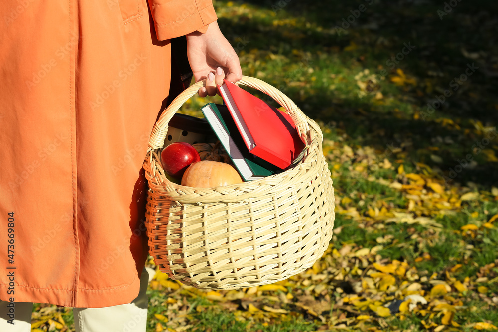 在户外拿着装有水果、蔬菜和书籍的野餐篮子的女人