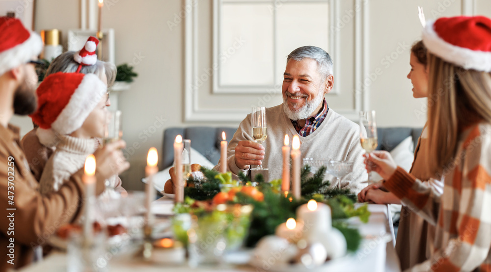 幸福的多代家庭在餐桌上戴着圣诞帽，说圣诞祝酒词，碰杯