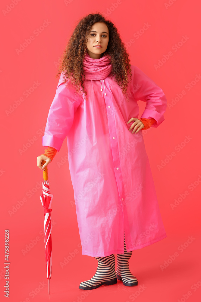 穿着粉色雨衣、围巾和胶靴，红色背景上带着雨伞的年轻非裔美国女性