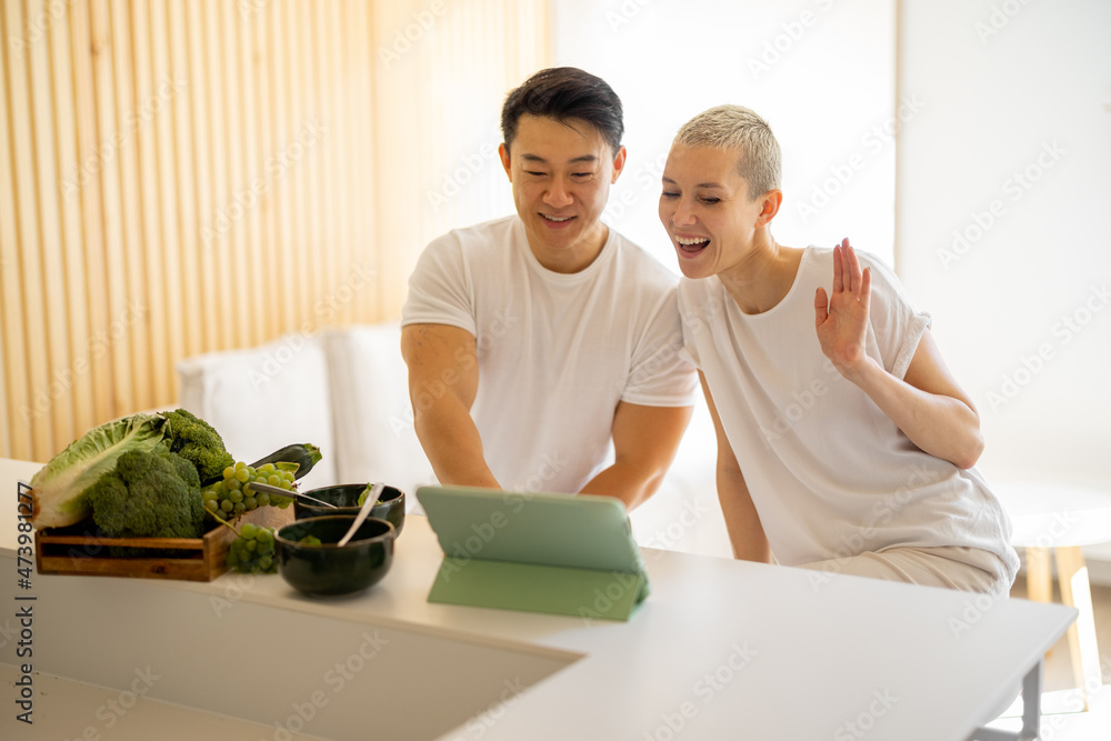 微笑的多种族夫妇在家里用数字平板电脑进行视频通话。家庭生活的概念