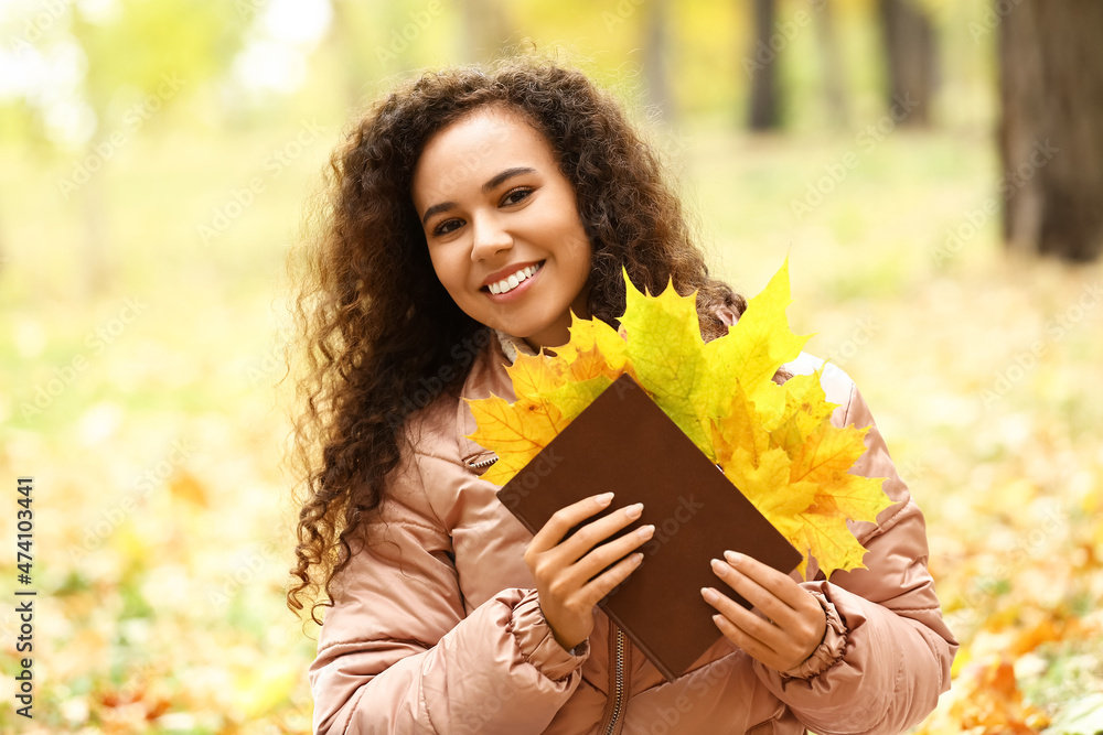美丽的非裔美国妇女在秋季公园拿着枯叶书