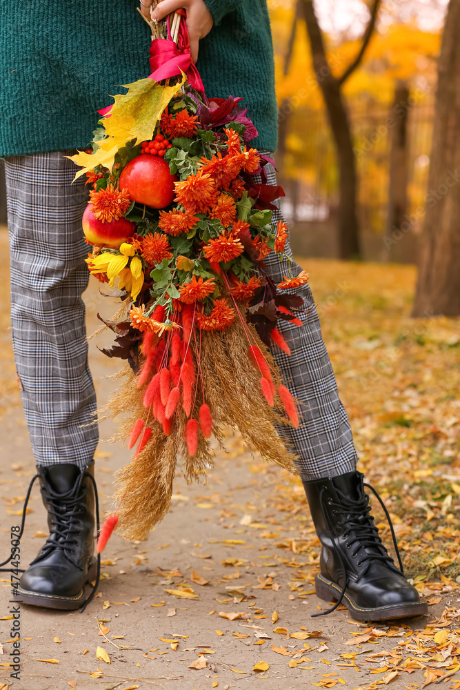 秋天公园里，一位年轻女子穿着解开鞋带的靴子，手里拿着花束，特写