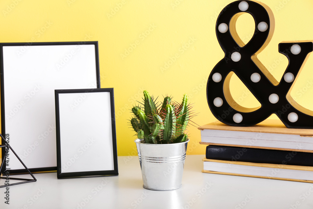 盆栽仙人掌、书籍、空相框和彩色墙上桌子上的装饰