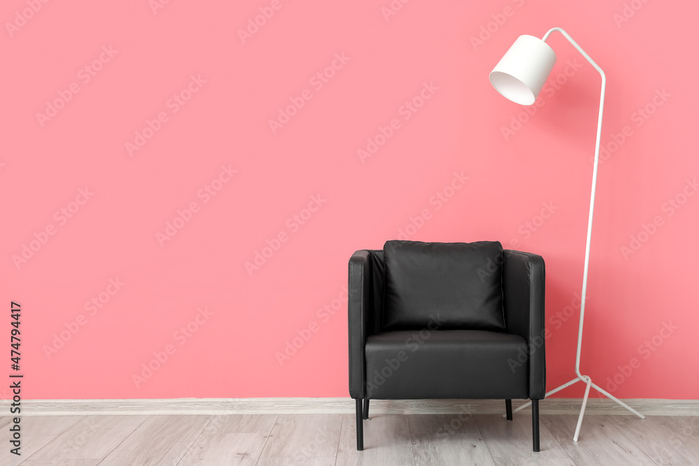 粉色墙壁附近的现代黑色扶手椅和白色立灯