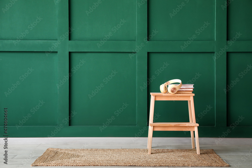 Wooden step stool with headphones and books near green wall