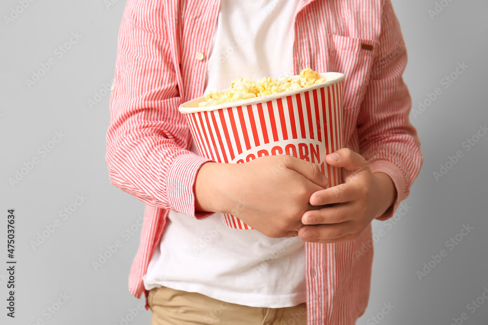 Little boy with bucket of tasty popcorn on light background