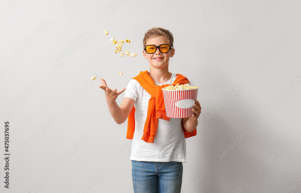 Little boy in eyeglasses throwing tasty popcorn on light background