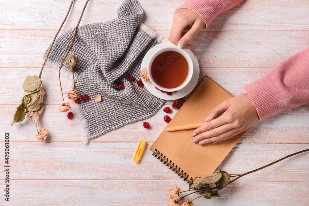 女性双手拿着一杯芳香的茶，笔记本和干花，浅木背景，特写