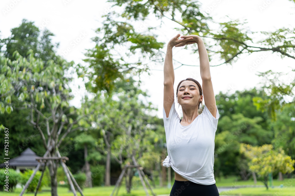 亚洲年轻运动女性在公园锻炼前伸展身体热身。