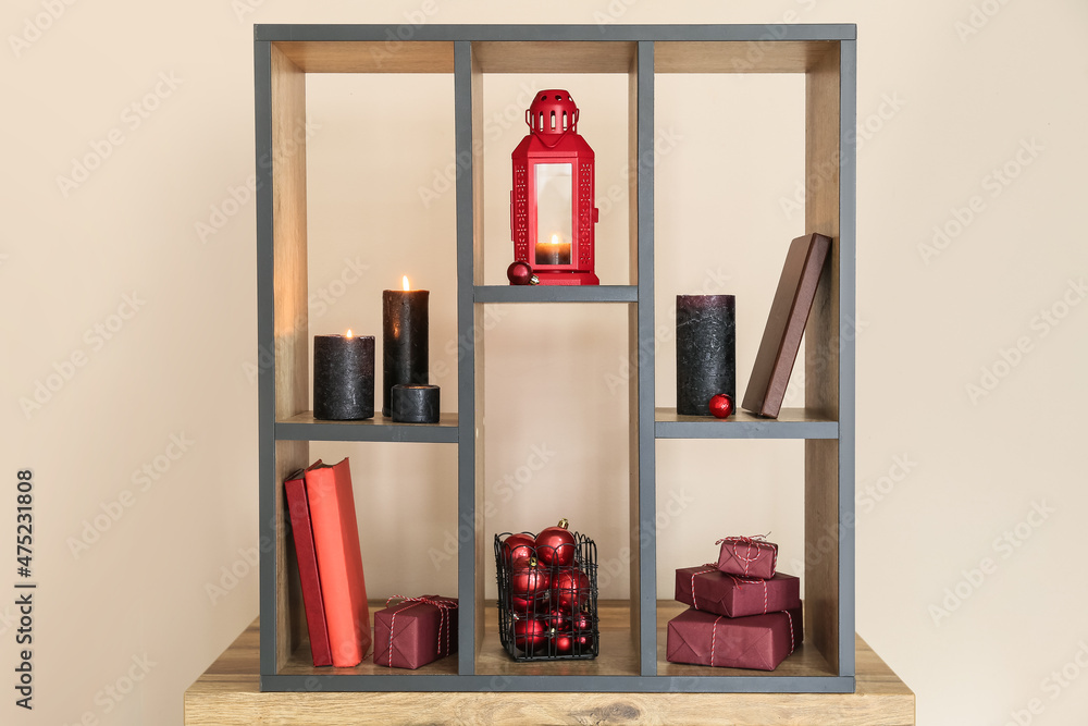 带灯笼、燃烧的蜡烛、圣诞礼物和彩墙附近的装饰品的木制架子单元