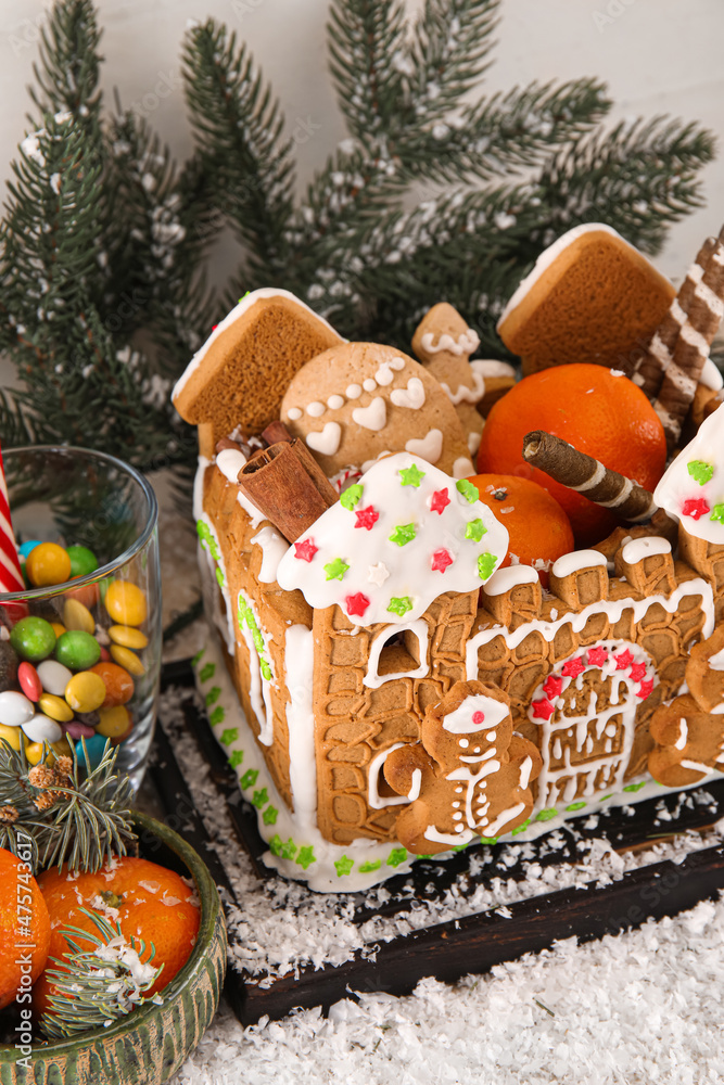 Board with beautiful gingerbread house, tangerines, snow and treats on table