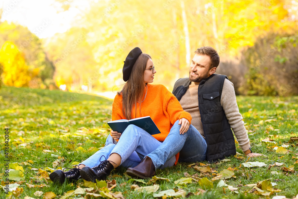秋天公园里，年轻的夫妇拿着书坐在草地上