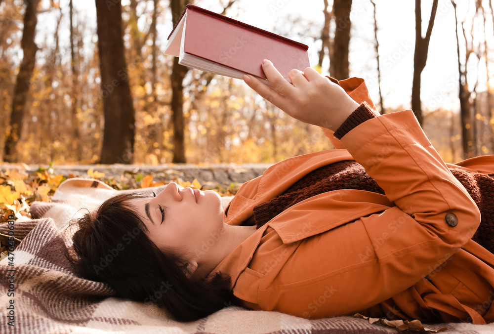 在秋天公园里读格子书的年轻女人