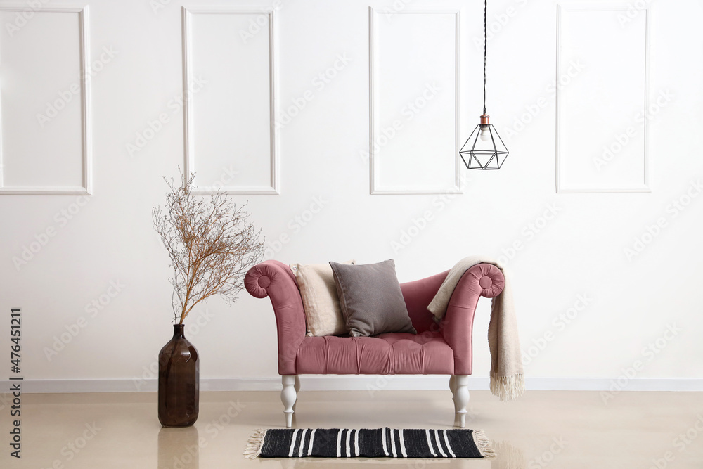 粉色扶手椅，带枕头、格子布、花瓶和靠近光墙的树枝